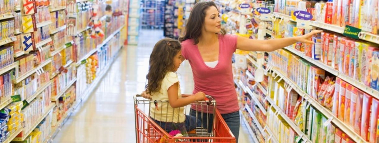 Mutter mit Kind im Einkaufswagen zwischen Supermarktregalen Mutter mit Kind im Einkaufswagen zwischen Supermarktregalen